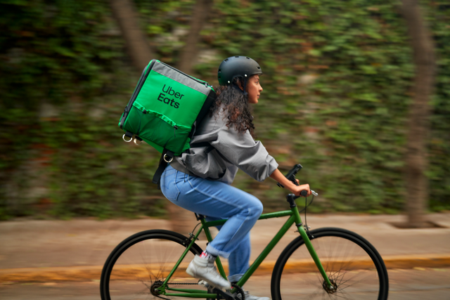 Woman delivering Uber Eats by bicycle. Green wall in the background!