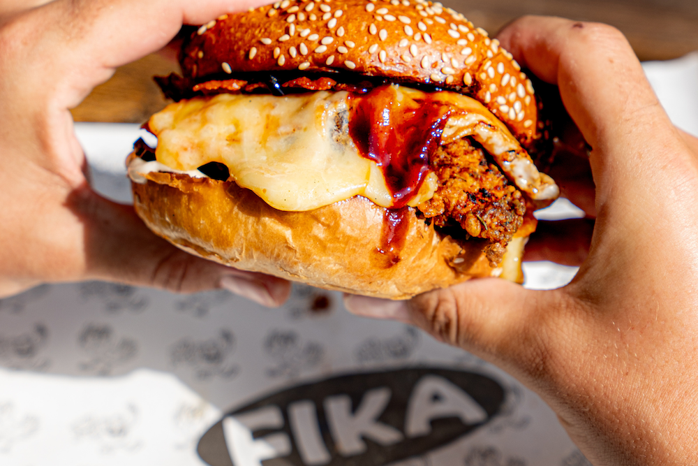 Two hands holding a burger oozing with cheese and sauce